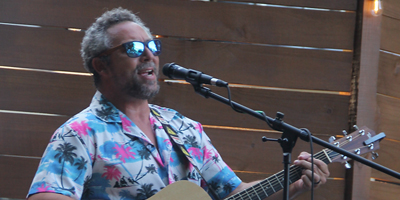 Man with sun glasses playing a guitar and singing into a microphone.